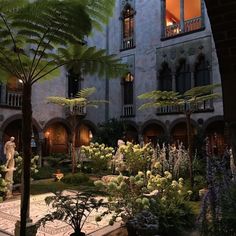 the courtyard of an old building with many plants and flowers around it, at night