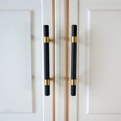 two black and gold handles are on the white door with wooden poles in front of them