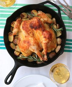 a roasted chicken in a skillet with potatoes and rosemary