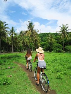 two people riding bikes on a dirt path in the middle of a lush green field