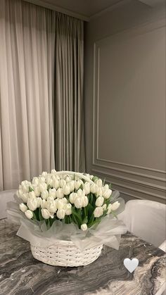 a basket filled with white tulips sitting on top of a table next to a window