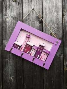 a purple frame hanging on the side of a wooden fence with small houses in it