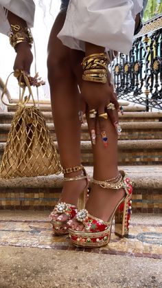 a woman in high heels with gold jewelry on her feet and handbag behind her