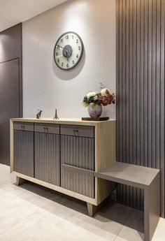 a clock mounted to the side of a wall next to a wooden cabinet and bench