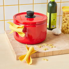 a red pot sitting on top of a wooden cutting board next to a bottle of wine