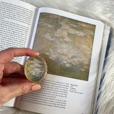 a person holding an open book with water lilies on it and a painting in the background