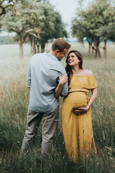 a pregnant couple standing in tall grass together