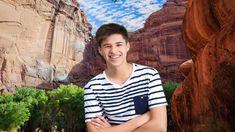 a young man standing in front of a mountain with his arms crossed and looking at the camera