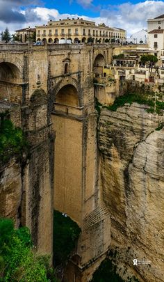 an old stone bridge over a river next to a tall building on top of a cliff