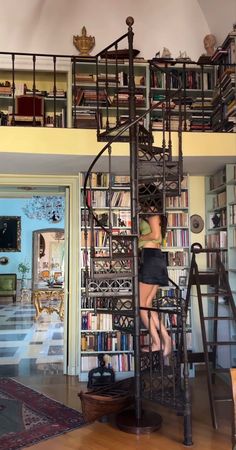 a woman standing on top of a spiral staircase in front of a bookshelf