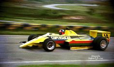 a man driving a yellow race car down a road next to a lush green hillside