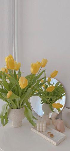 yellow tulips are in a white vase next to a mirror on a table