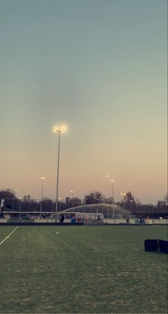 an empty soccer field at dusk with the lights on and people playing in the background