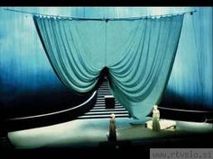 a woman standing in front of a blue curtain with stairs leading up to the top