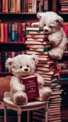 two white teddy bears sitting on top of a stack of books