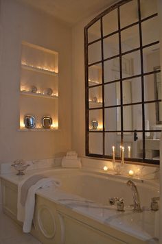 a bathtub with candles on the wall and shelves in front of it that are lit up