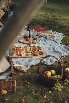 an outdoor picnic with food and wine on the table, along with other items in wicker baskets