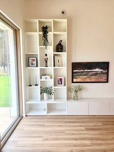 a living room filled with lots of white shelves next to a sliding glass door window