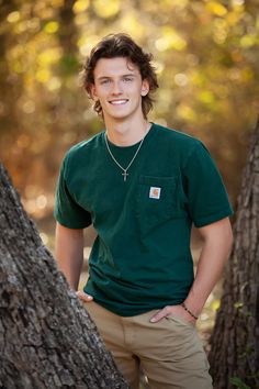 a young man standing in front of a tree with his hands on his hips and smiling at the camera