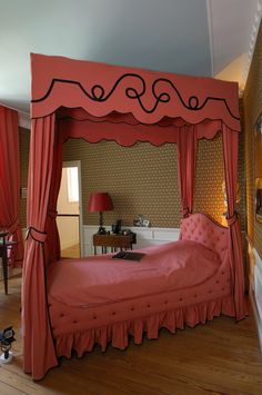 a bedroom with a pink canopy bed and red drapes on the top of it