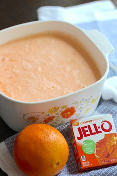 an orange sitting next to a bowl of jello and a small box of candy