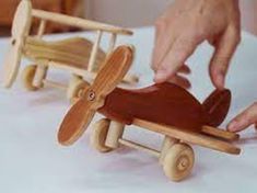 two wooden toy airplanes are being held by someone's hand over a table with white linen