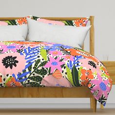 a bed with pink and green floral comforter on it, next to a white wall