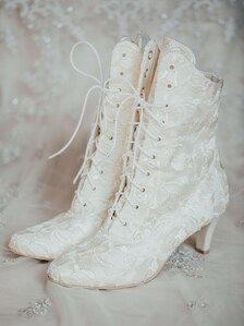 a pair of white high heeled boots on top of a bed of lace and beads