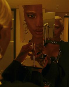 a woman is looking at her reflection in the mirror while another person holds up an object