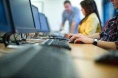 two people sitting at a desk with computers in front of them and one person typing on the keyboard