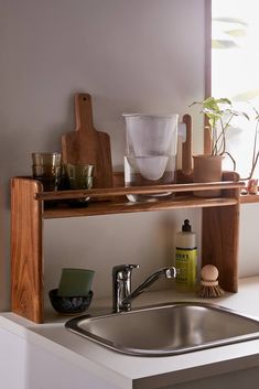 a kitchen sink under a wooden shelf with utensils and other items on it