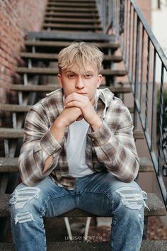 a young man sitting on some steps with his hands clasped to his chin and looking at the camera