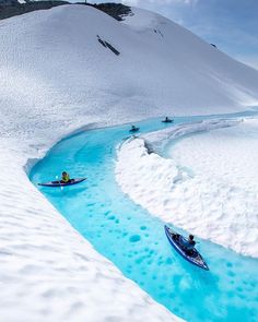 two people are kayaking down a blue stream in the middle of snow covered mountains