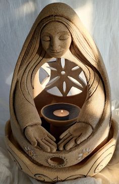 a candle holder made out of clay with hands holding a lit candle in it and an intricate design on the base