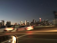 two cars driving down the road in front of a city skyline