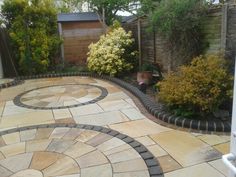 an outdoor patio with stone pavers and circular design on the ground, surrounded by shrubbery