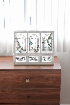 a stained glass window sitting on top of a wooden dresser next to a white curtain