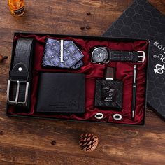 an assortment of men's accessories in a black box on a wooden table next to a pine cone