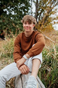 a young man sitting on top of a wooden log