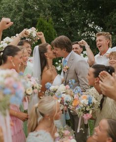 a group of people standing next to each other in front of a wedding cake and flowers