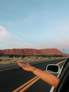 a woman is driving down the road with her hand out the window