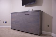 a flat screen tv mounted on the wall above a dresser in a room with carpeted flooring