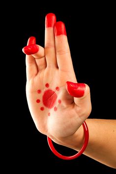 a woman's hand with red nail polish holding her fingers up in the air