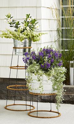 three metal buckets filled with flowers sitting on the side of a house