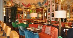 the interior of a fancy restaurant with orange and green velvet booths, gold chandeliers, and colorfully decorated walls