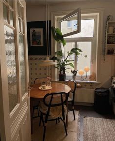 a dining room table and chairs in front of a window with a potted plant