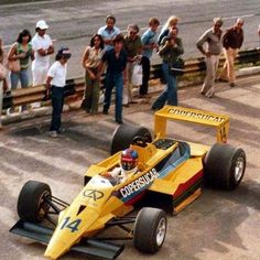 a man driving a yellow race car on top of a track next to people watching