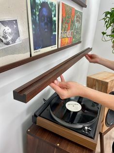 a person is touching a record player on a shelf with pictures hanging above it and another hand reaching out to touch the turntable