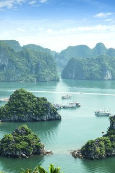 several small islands in the water surrounded by trees and mountains, with boats floating on them