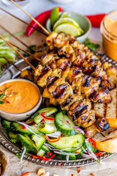 grilled chicken skewers on a platter with salad and dipping sauce